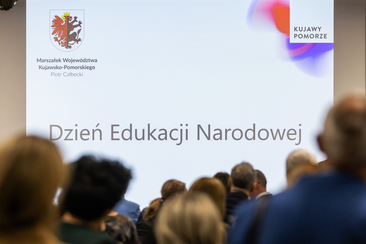 widownia widziana z tyłu, w tle widnieje prezentacja Dzień Edukacji Narodowej z logotypami Województwa Kujawsko-Pomorskiego